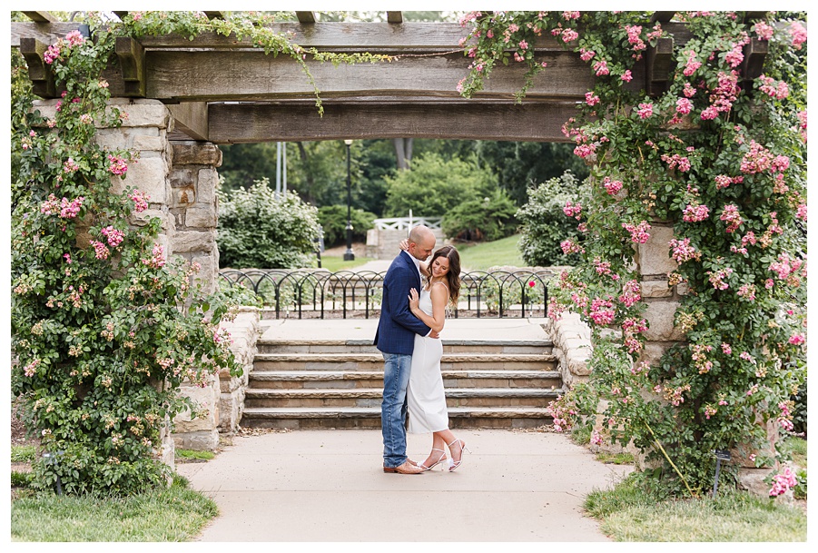Engaged couple embracing beneath a floral arch during a Loose Park engagement session in Kansas City, Missouri