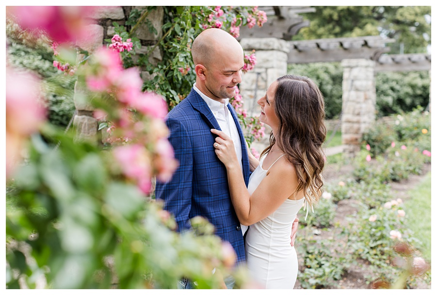 Engaged couple embracing beneath a floral arch during a Loose Park engagement session in Kansas City, Missouri